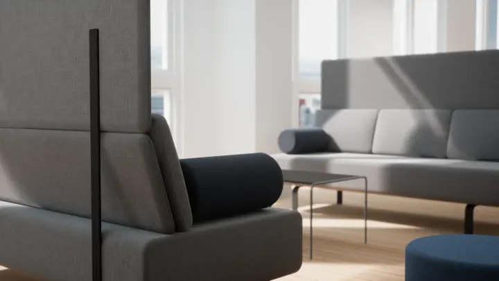 Close-up of grey upholstered lounge sofas with a dark bolster cushion, a low table and a blue stool in sunlight
